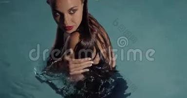 穿着黑色裙子的女人站在游泳池里摆姿势，化妆和口红，4K